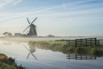 Classic dutch windmill along the water of a canal in the polder landscape of Holland with fogbanks...