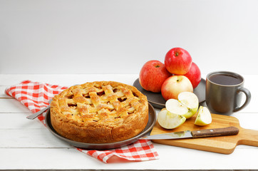 Homemade apple pie with lattice, apples and cup of tea on white wooden table. Angle view. Copyspace.