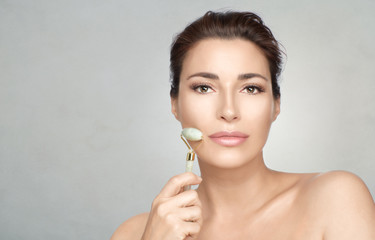 Attractive woman using face roller on cheek. Skin care and beauty treatment