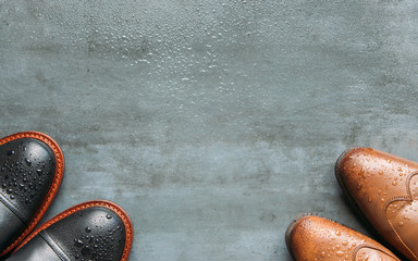 Top view of black and brown leather men boots with water drops on wet grunge navy blue background,...