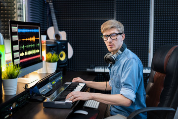 Young man with headphones looking at you while sitting in recording studio