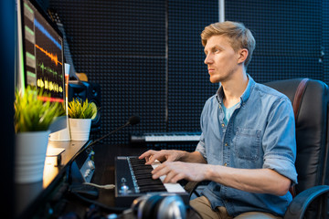 Young man looking at computer screen while pressing keys of piano keyboard