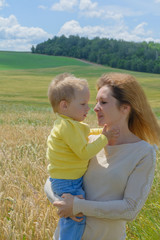 Mother hugging her child during walk. Mother and son cuddling. Picturesque landscape of field on background.