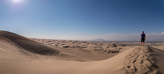 Panoramic landscape from a desert an a man standing alone over a dune on the right side. Ica, Peru