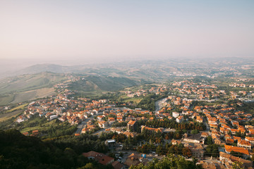 Fototapeta na wymiar View from the top of San Marino castle. San Marino suburban districts and Italian hills view from above. Panorama of San Marino and Italy from Monte Titano.