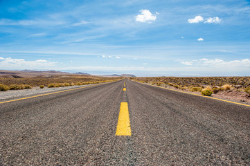 American empty desert asphalt road from low angle with mountains and clouds on background. South american highway in Atacama desert, Chile. Yellow striped road.