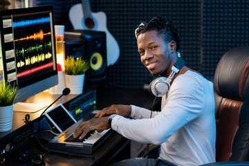 Happy young musician with headphones on neck working over new music by workplace