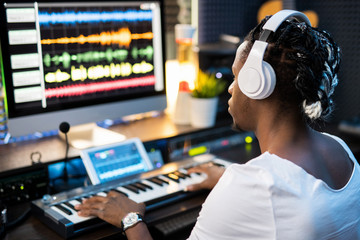 Young musician in headphones looking at sound waveforms on computer screen
