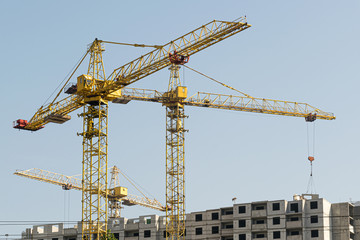 Several yellow high-rise construction cranes build multi-storey multi-apartment residential buildings using modern technologies of metal, concrete and brick according to the architectural design