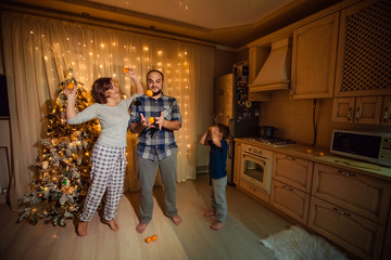 Family mom dad son in the New Year have fun in the kitchen at the Christmas Tree.