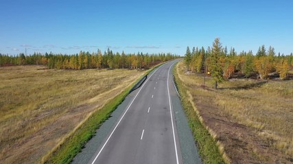 Flying over the road with a moving car on an autumn day in Northern Siberia