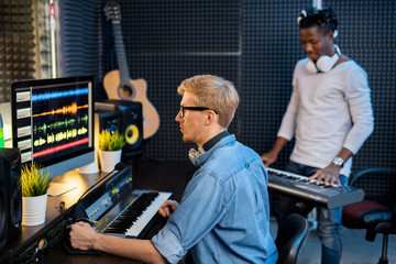 Serious man in denim shirt working with sound waveforms in studio of records