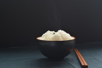 black bowl of rice with wood chopsticks on a black background