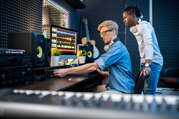 Young casual man adding volume while recording music with his African colleague
