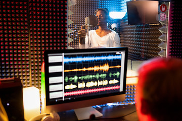 Young African-american man with headphones singing in sound recording studio