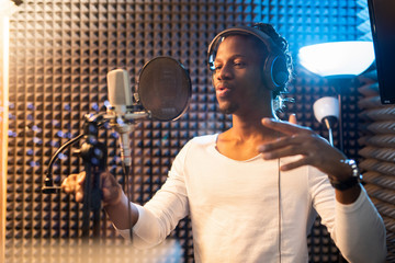 Young African man in white t-shirt and headphones performing songs in studio