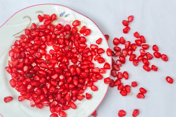 Pomegranate seeds placed in a plate with scattered seeds on white background