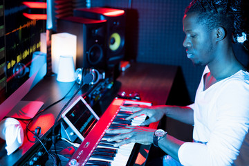 Young serious African-american man making new music while sitting in studio