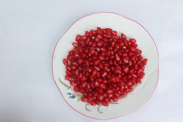 Pomegranate seeds placed in a plate with scattered seeds on white background