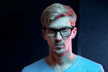 Serious young blond man of Caucasian ethnicity looking at you through eyeglasses