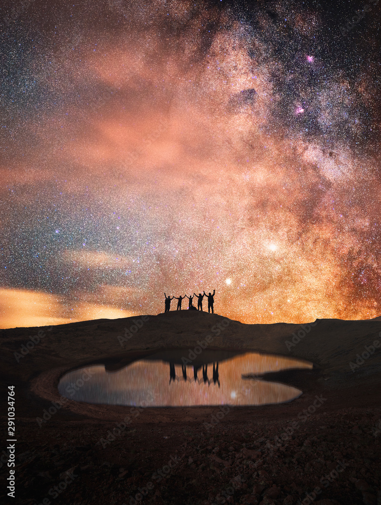 Wall mural silhouette of a group of people standing on a mountain. behind their beautiful starry sky and the mi