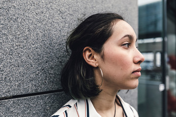 Side view of sas young woman face leaning on wall in the city.
