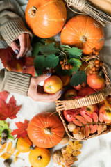 Woman taking apple from basket standing on table among ripe pumpkins and leaves