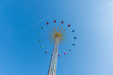 high flying carousel against strait blue sky and airplane line at summertime on a large pole and 16 colored stools in blue red green and pink lovely whether