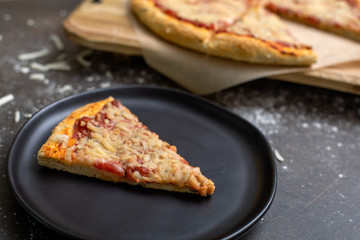 Homemade Pizza with Vegan Cheese on a Black Background; One Slice Isolated in Front on Black Plate