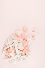 Fototapeta na wymiar Reusable shopping net bag with white and pink knitted hearts on pastel background. Top view of eco friendly mesh shopping cotton bag. Ecological, Zero waste, No plastic concept