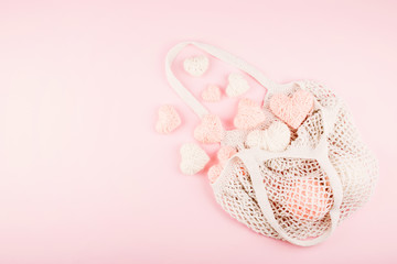 Reusable shopping net bag with white and pink knitted hearts on pastel background. Top view of eco friendly mesh shopping cotton bag. Ecological, Zero waste, No plastic concept