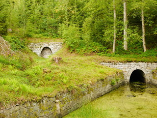 Artificial pond with archway, with further archway above and birch trees behind in Harz, Germany