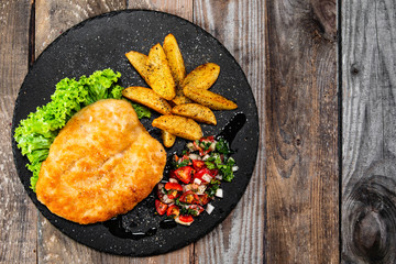 Fried pork chop, baked potatoes and vegetables on black stone plate