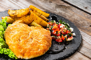 Fried pork chop, baked potatoes and vegetables on black stone plate