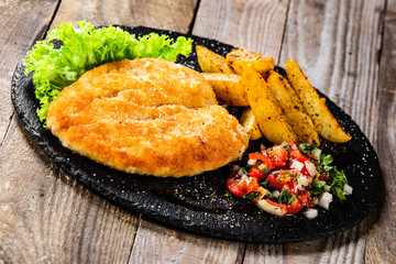 Fried pork chop, baked potatoes and vegetables on black stone plate