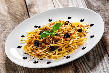 Pasta with black olives and chilli on wooden table