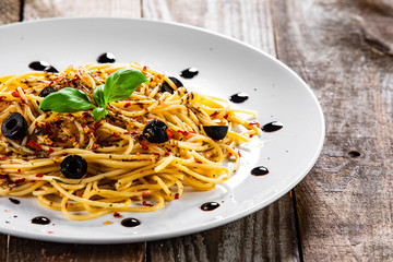 Pasta with black olives and chilli on wooden table