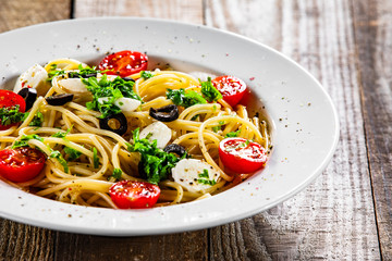 Pasta with cherry tomatoes and mozzarella cheese on wooden table