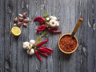 Red hot sauce, garlic, lemon, red pepper and spices on a black wooden  table. Top view. 