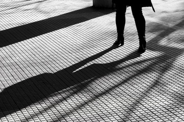 Blurry silhouette shadow of legs of a woman in high heels walking alone on tiled pedestrian walkway