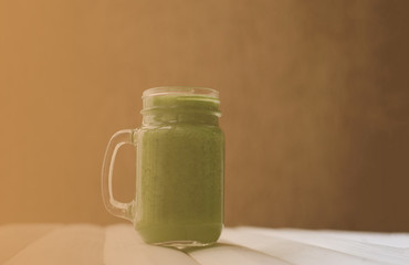 Green vegetable smoothie in glass mason jar on white wooden table indoor. Place for text. Healthy, vegan concept