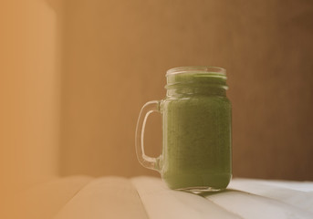 Green vegetable smoothie in glass mason jar on white wooden table near window indoor. Place for text. Healthy, vegan concept