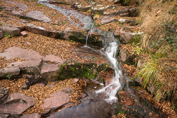 Beautiful autumn colors of cascading mountain creek and rocky bank covered with red leaves
