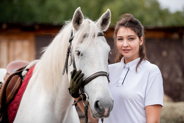 Young woman touching muzzle of purebred racehorse in natural environment