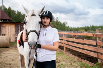 Young sportswoman in activewear standing by white purebred racehorse
