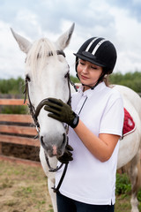 Young active female cuddling muzzle of white purebred racehorse