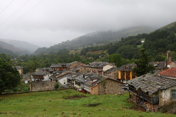 Fototapeta na wymiar Village and mountains with gray sky, fog and rain