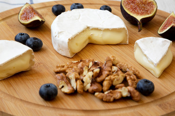 Camembert cheese with figs, blueberries and walnuts on a bamboo board over white wooden background, side view. Food for wine. Close-up.