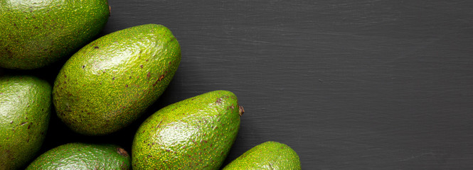 Whole avocados on a black surface, top view. From above, overhead, flat lay. Copy space.