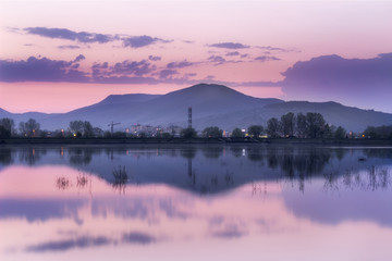 Distant mountain and city, blue hour lake mirror reflection in a calm water of vivid purple sky 